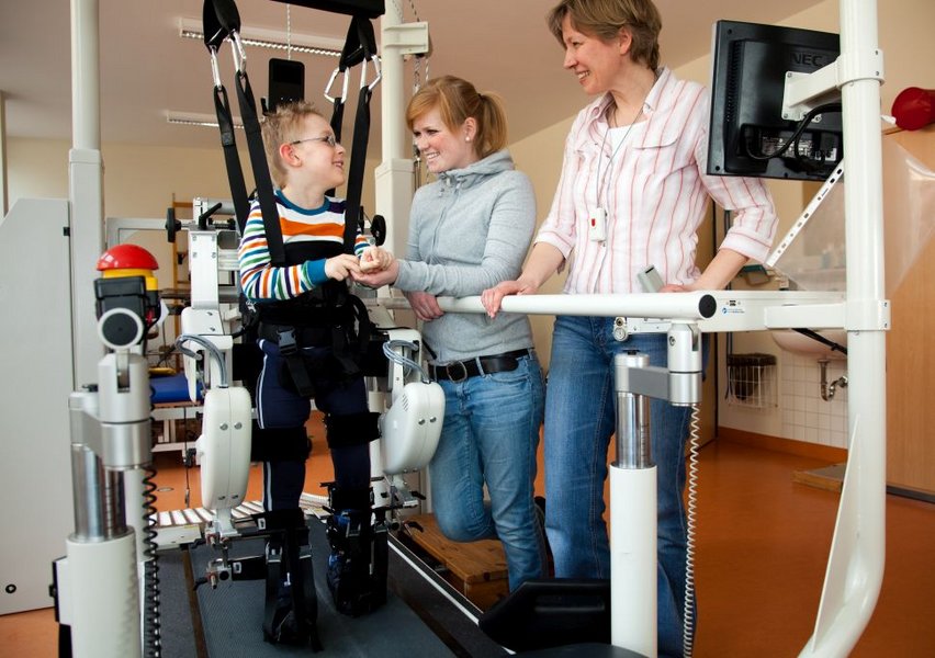Junge im Lokomat mit Therapeutinnen
