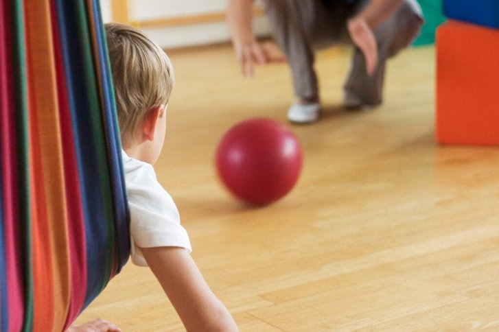 Nahaufnahme eines Jungen der in Bauchlage in einer Haengematte liegt und sich auf einen Ball zubewegt