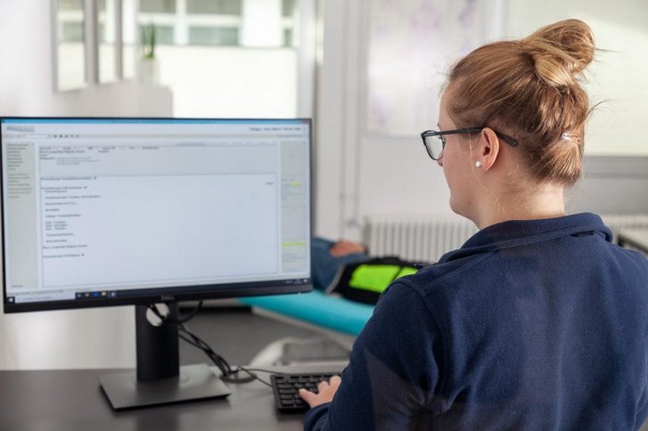 Eine Physiotherapeutin sitzt am PC und erstellt einen individuellen Behandlungsplan für einen Patienten in der Physiotherapie Abteilung des VITREA Rehazentrum Karlsruhe