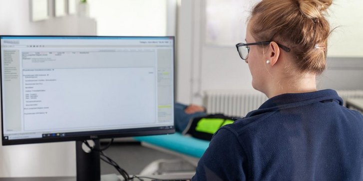 Eine Physiotherapeutin sitzt am PC und erstellt einen individuellen Behandlungsplan für einen Patienten in der Physiotherapie Abteilung des VITREA Rehazentrum Karlsruhe